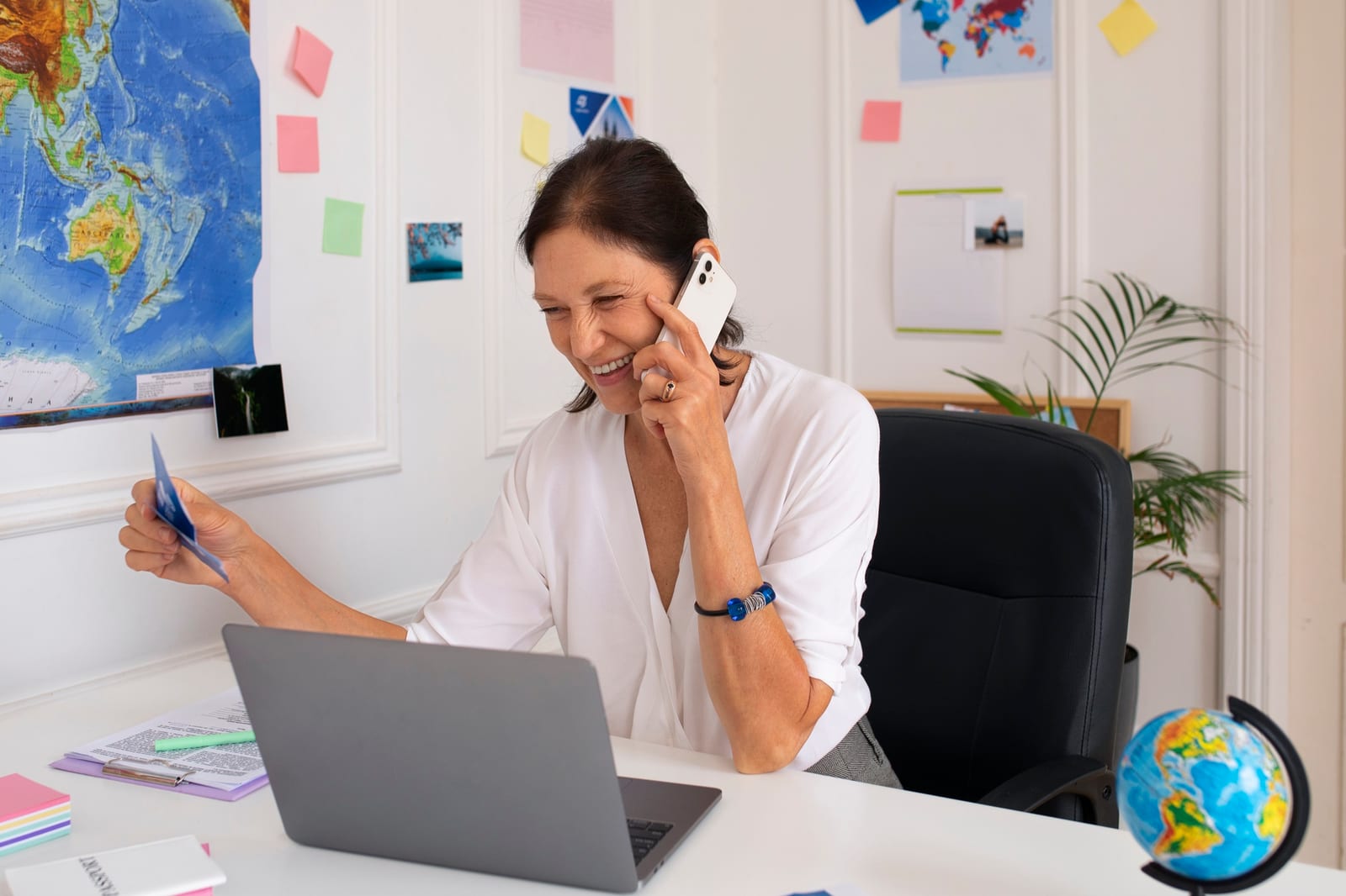 Consultora de viagens atende ao telefone segurando um cartão diante do notebook.